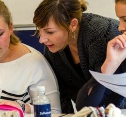 Docent helpt twee studenten met studiemateriaal.
