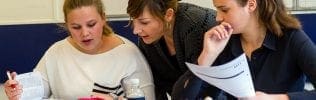 Docent helpt twee studenten met studiemateriaal.