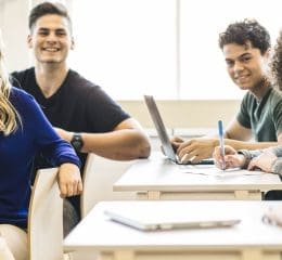 Groep studenten aan tafel met laptops en notitieblok.