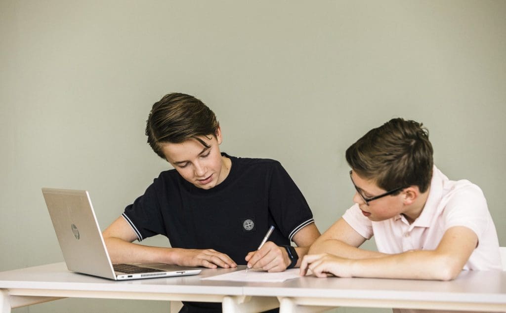 Twee jongens werken samen aan een opdracht met een laptop.