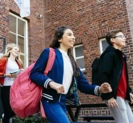 Drie brugklassers lopen lachend een schoolgebouw binnen.