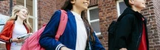Drie brugklassers lopen lachend een schoolgebouw binnen.