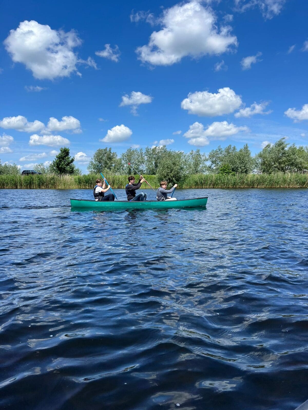 Drie mensen kanoën op een meer onder een blauwe hemel.