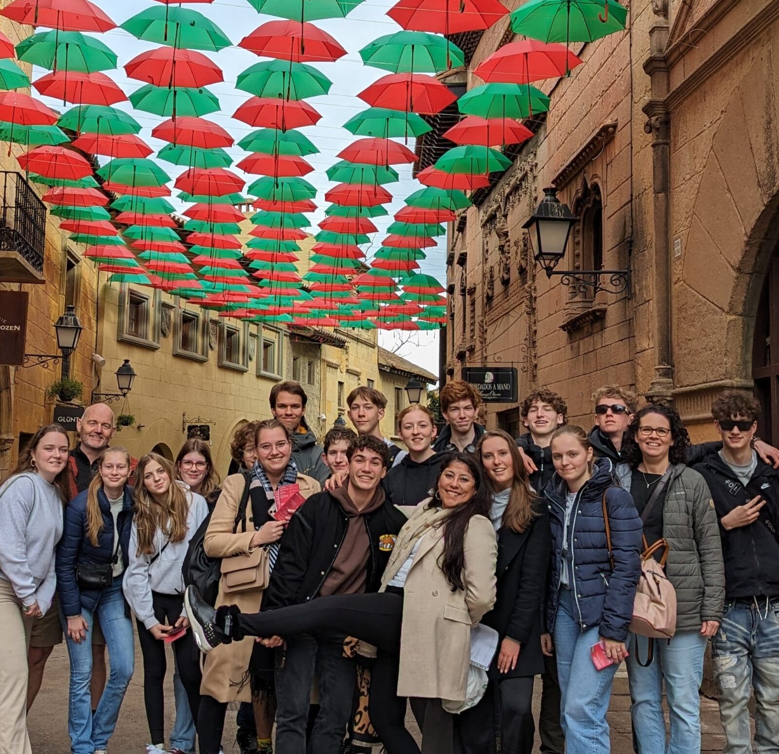 Groep studenten en docenten onder kleurrijke paraplu's in een straat.