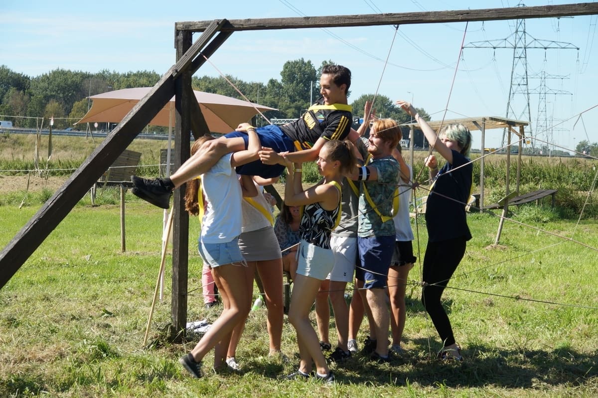 Groep kinderen helpt elkaar bij een touwparcours.