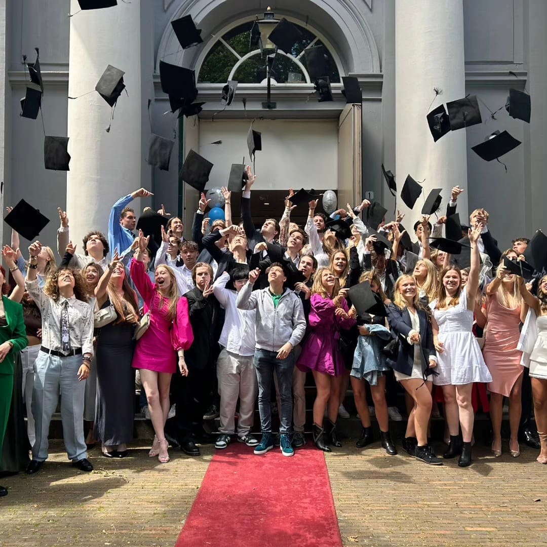 Groep studenten gooit afstudeerhoeden in de lucht.