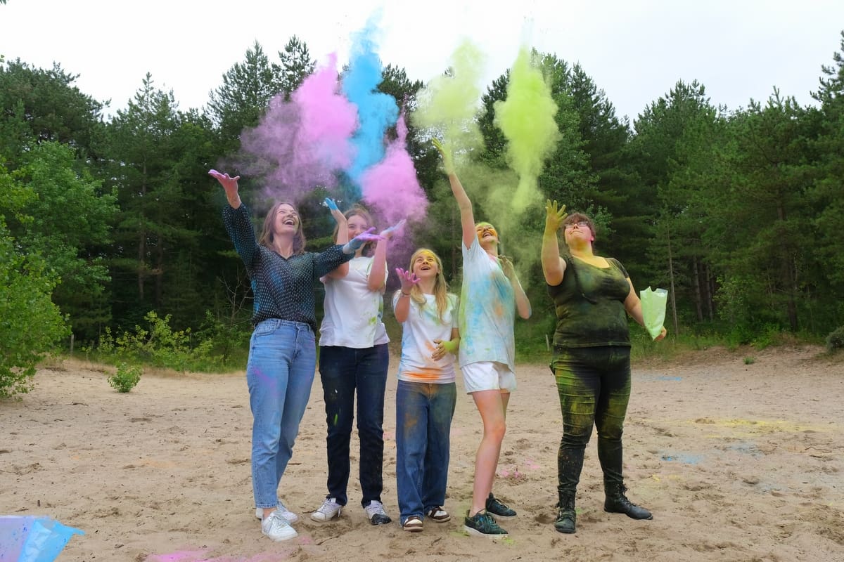 Groep mensen gooit gekleurd poeder in de lucht.