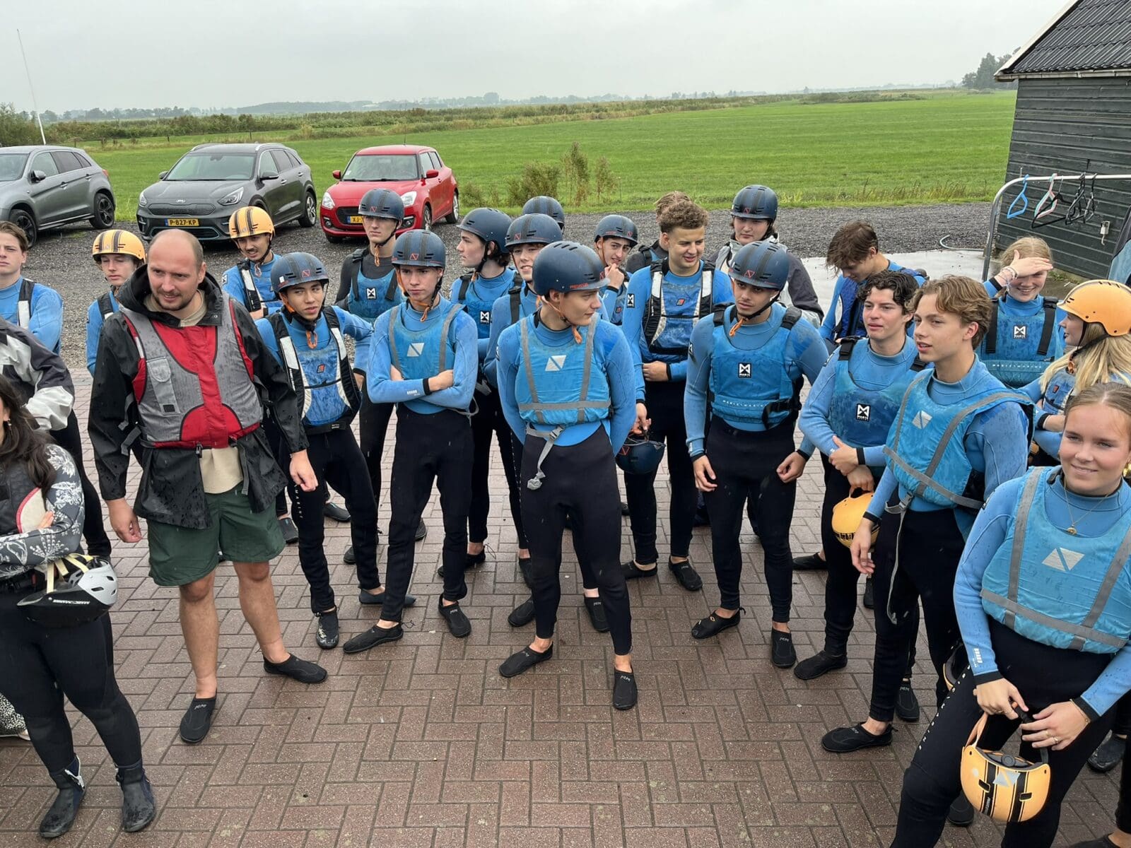 Groep studenten in wetsuits klaar voor watersportactiviteit.