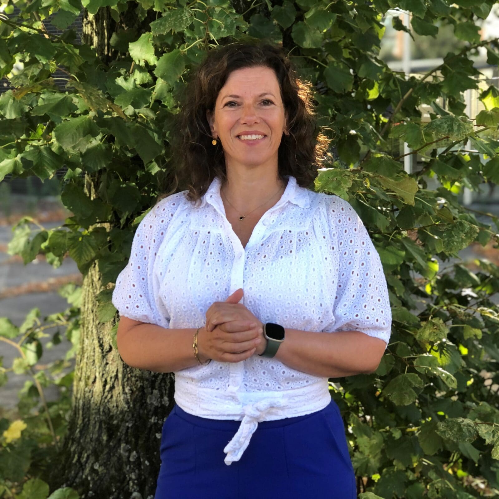 Portret van een lachende vrouw voor een boom.