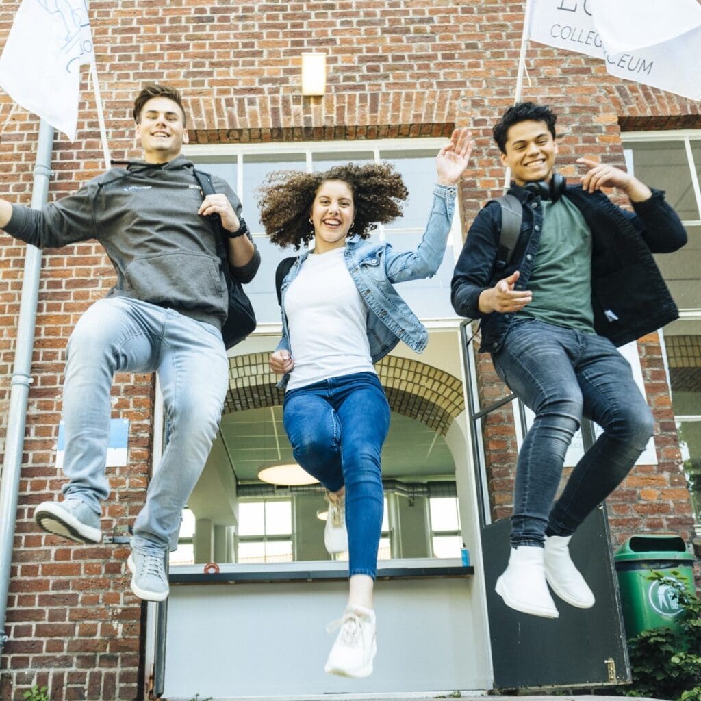Drie studenten springen voor een schoolgebouw.
