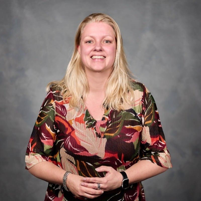 Portret van een lachende vrouw in kleurrijke blouse.