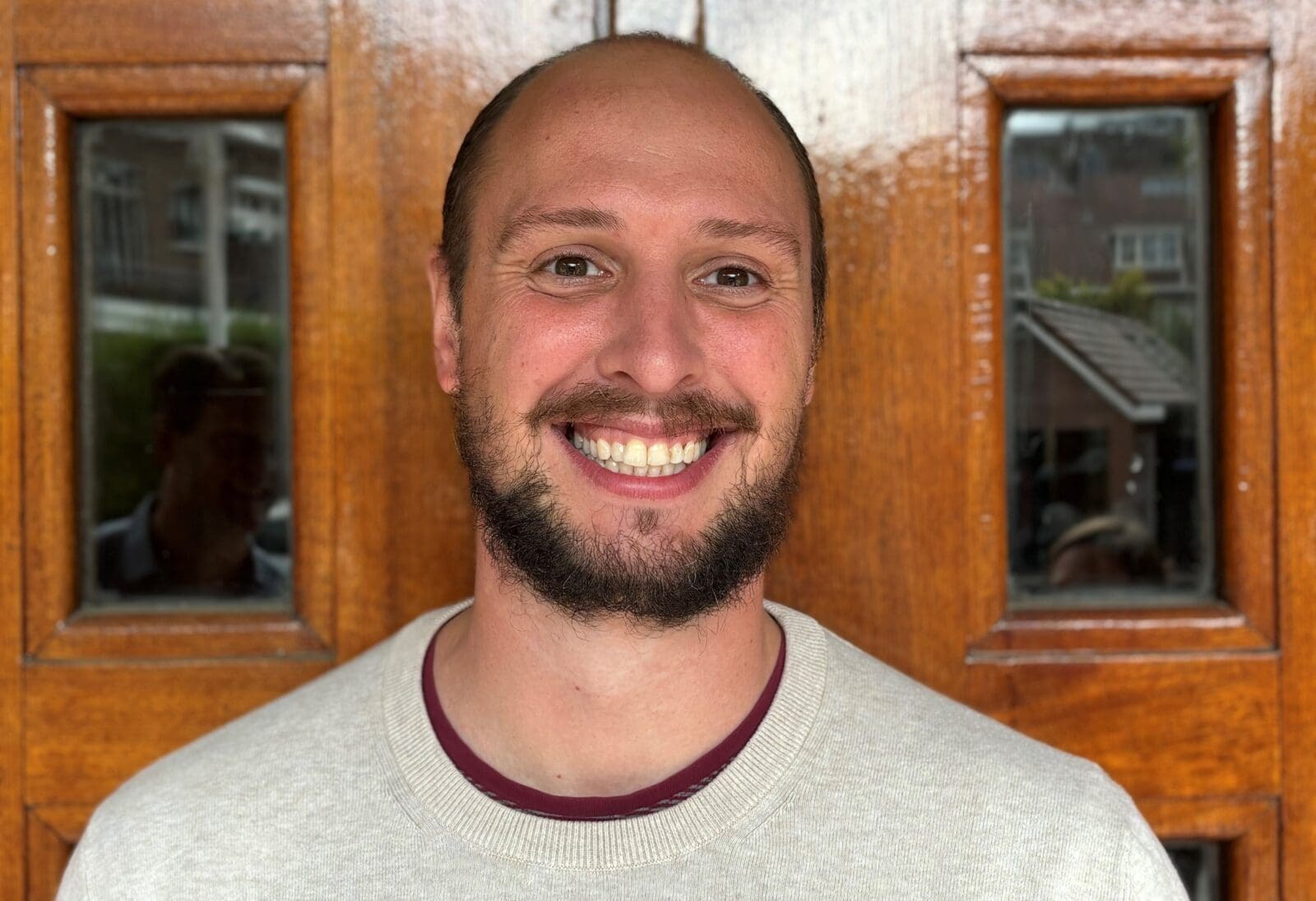 Portret van een lachende man voor een houten deur.