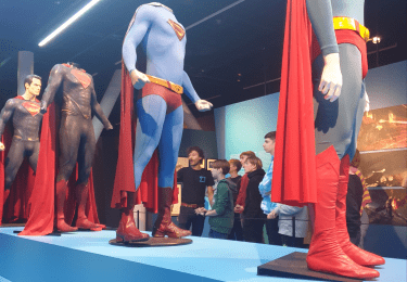 Superman kostuums tentoongesteld in een museum met bezoekers.