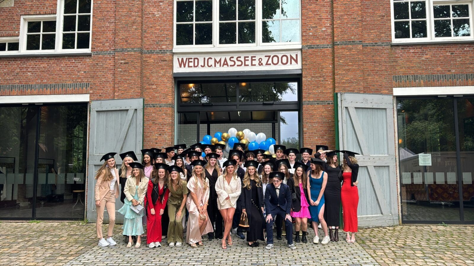 Groep studenten in afstudeerkleding voor gebouw Luzac Arnhem.