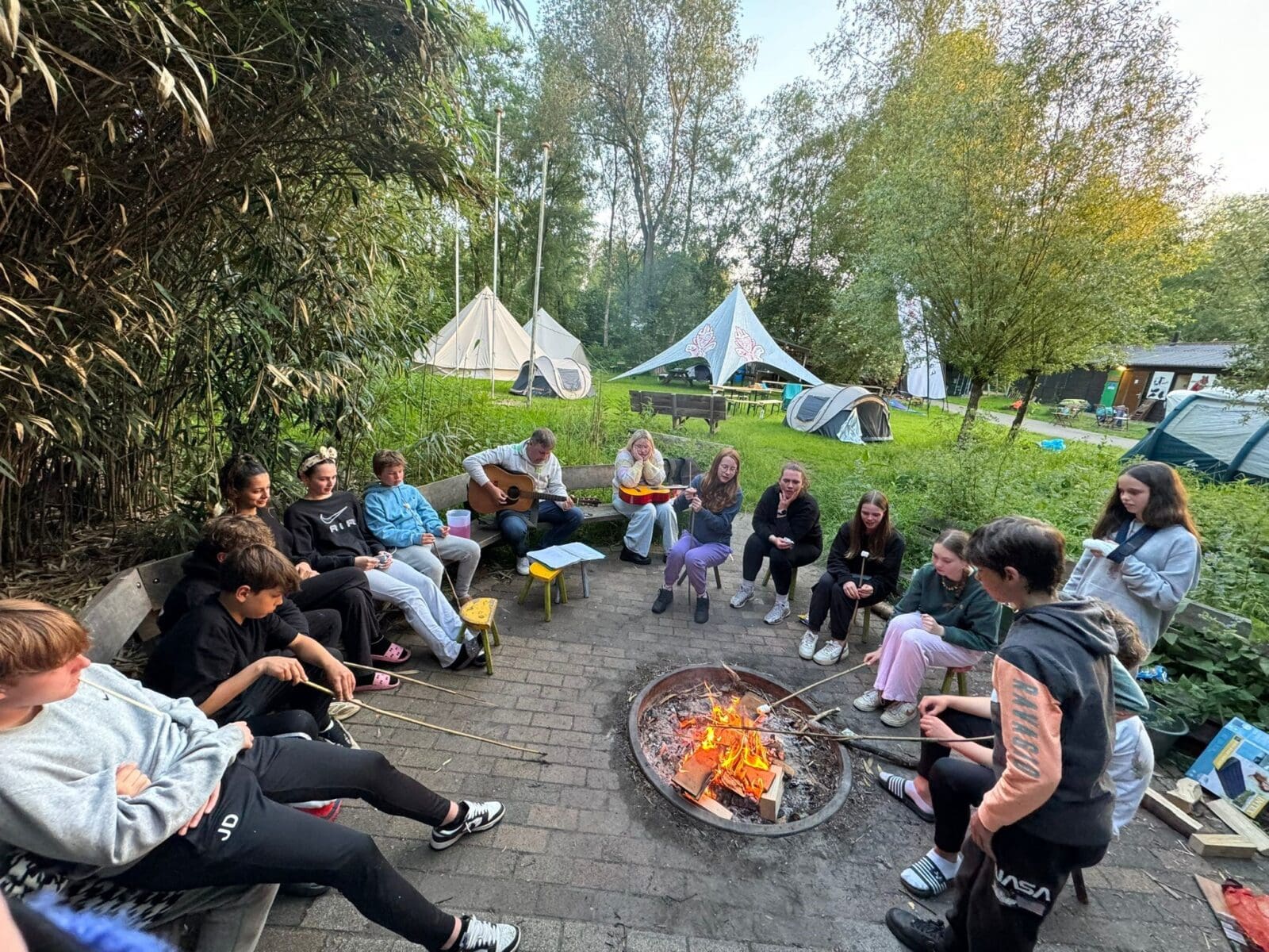 Groep studenten rond een kampvuur tijdens een kamp.