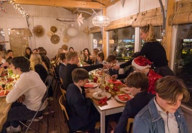 Kerstviering met studenten aan een feestelijk gedekte tafel.