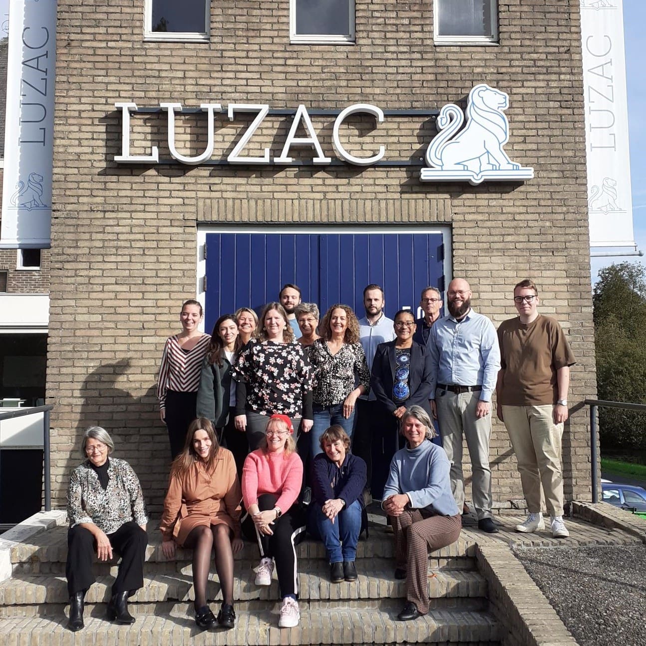 Groepsfoto van het team van Luzac Breda voor het gebouw.