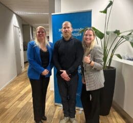 Twee vrouwen en een man poseren voor een foto in een kantooromgeving.