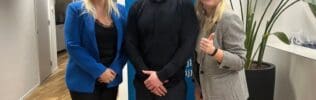 Twee vrouwen en een man poseren voor een foto in een kantooromgeving.